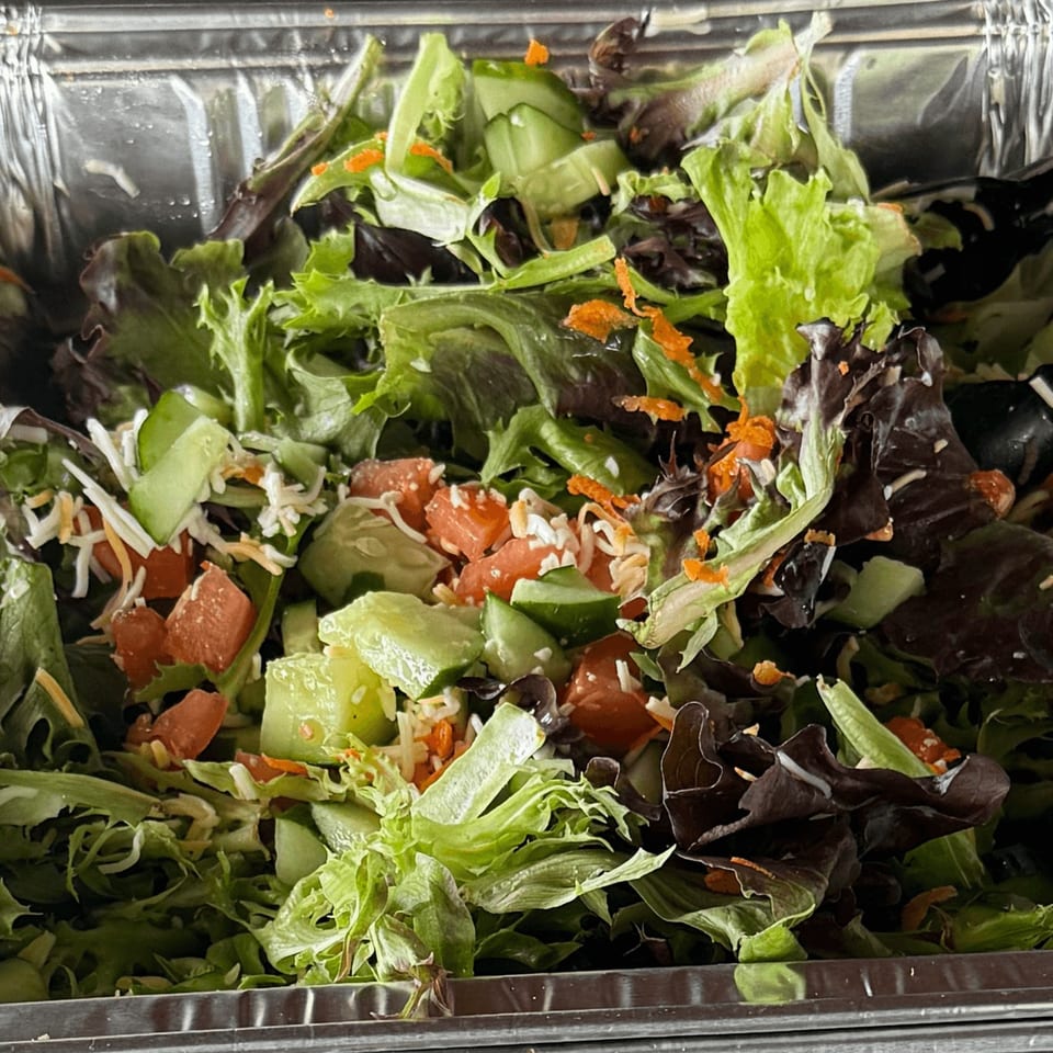 Fresh Da Kane's Kitchen side salad with mixed greens, tomatoes, cucumbers, shredded cheese, and carrots.