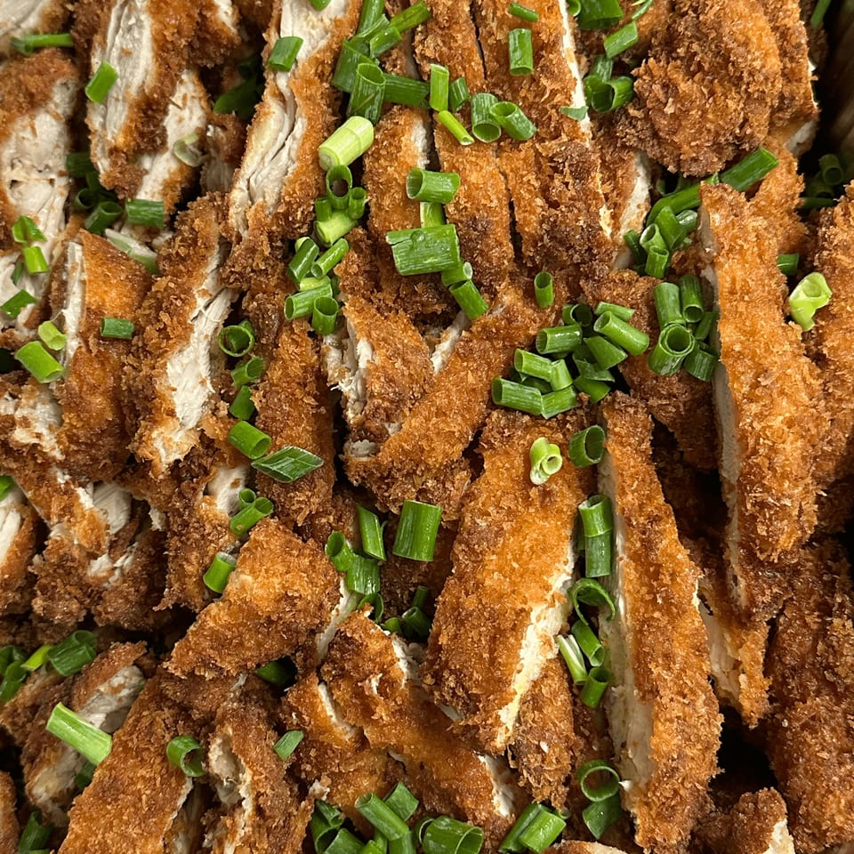 Crispy fried chicken cutlets, sliced and generously topped with fresh green onions.