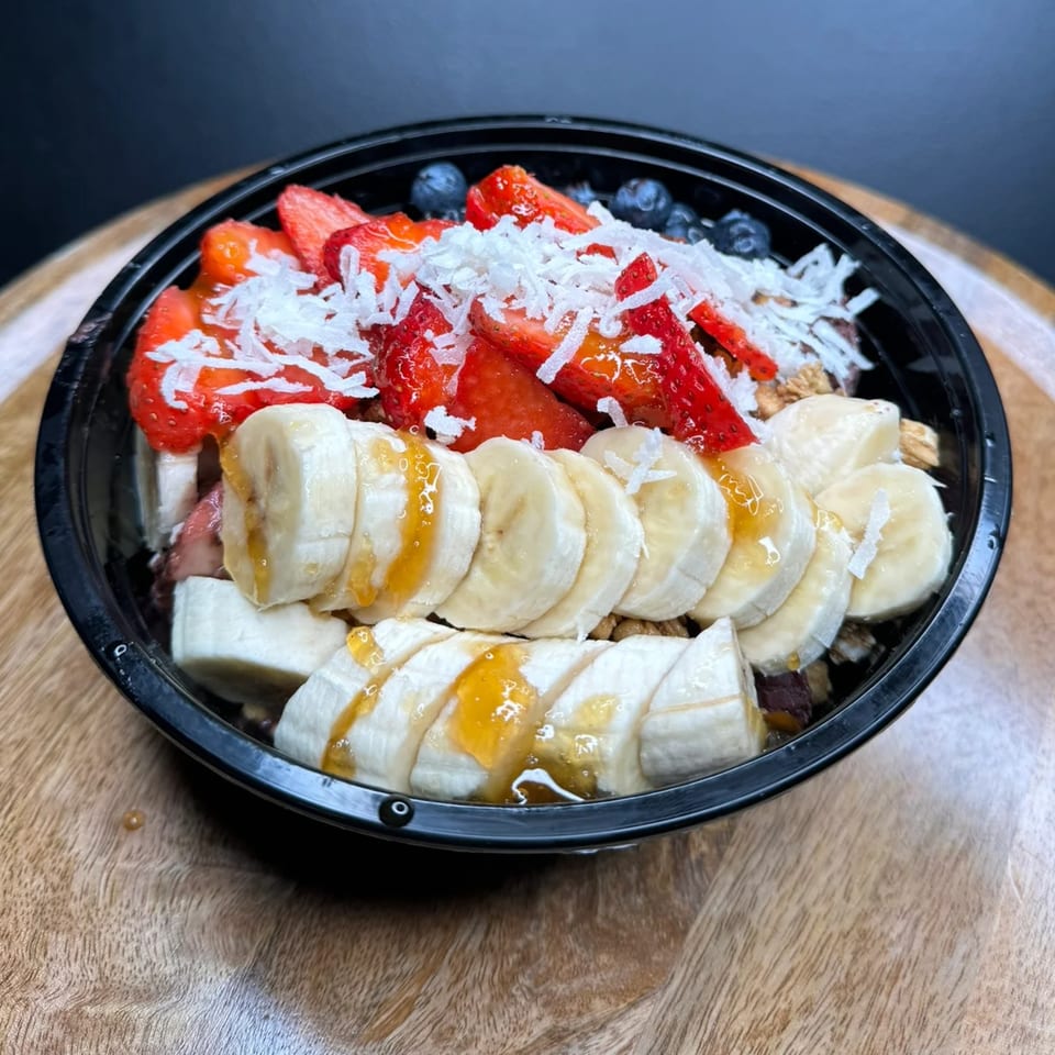 A Da Kane's Kitchen acai bowl with strawberries, blueberries, bananas, coconut flakes, and honey.