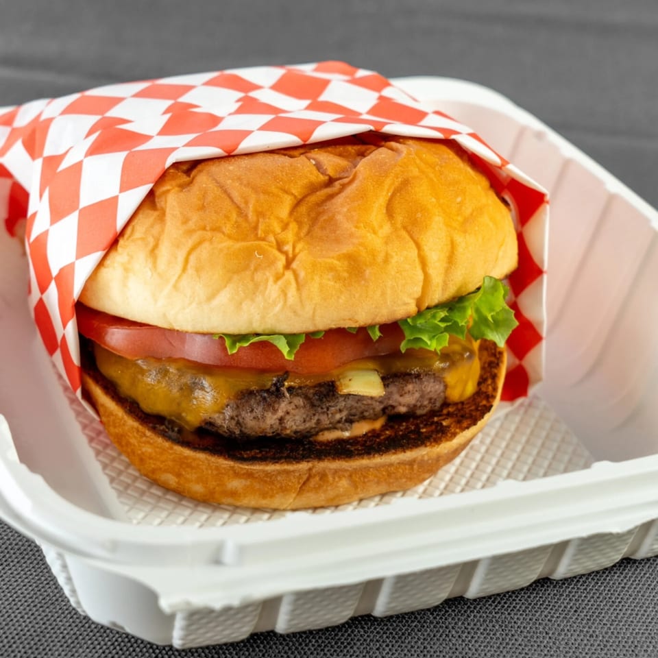 A Da Kane's Kitchen cheeseburger with lettuce and tomato, wrapped in red and white checkered paper.