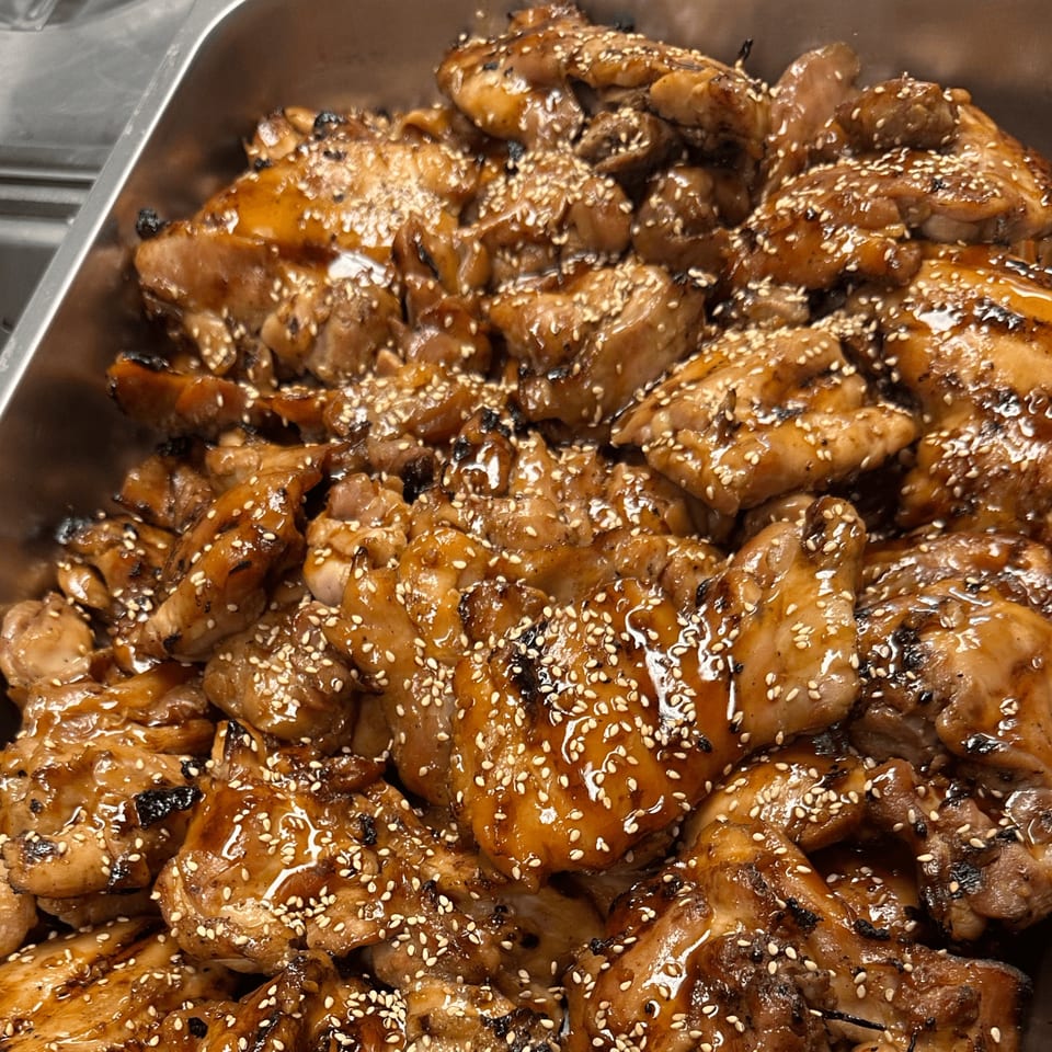 Close-up of Da Kane's Kitchen's American-style teriyaki chicken pieces, glistening with sauce and sesame seeds.