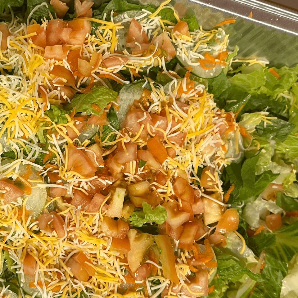 Close-up of a fresh green salad with shredded cheese, diced tomatoes, and cucumbers.