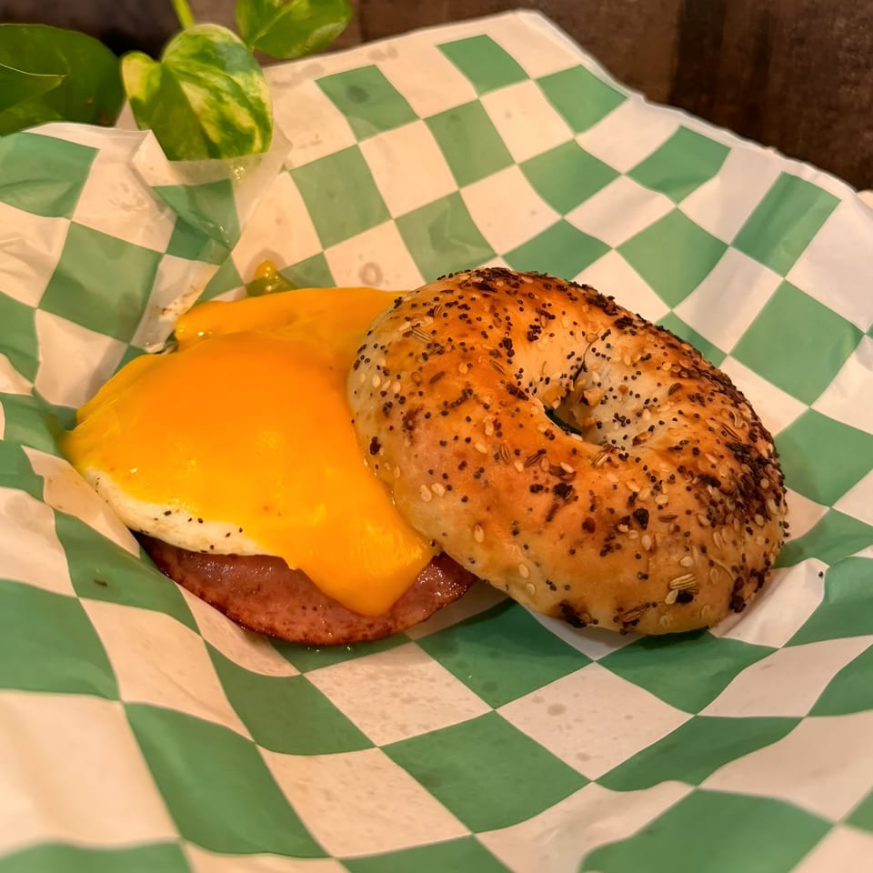 Da Kane's Kitchen's bagel sandwich with melted cheese, egg, and meat on checkered paper.