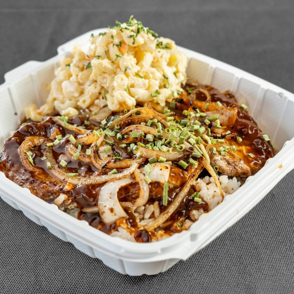 Da Kane's Kitchen's Loco Moco with gravy, onions, and macaroni salad in a white takeout container.